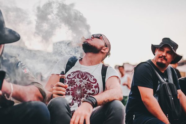 a man vaping in public and exhaling smoke in the air while others looking at him
